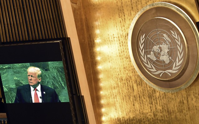 Image of Trump speaking set against a bright gold wall with a UN logo background