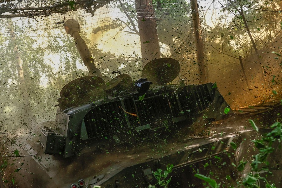 A large piece of mobile artillery fires, the shock creating a small cloud of dirt, leaves, and smoke.