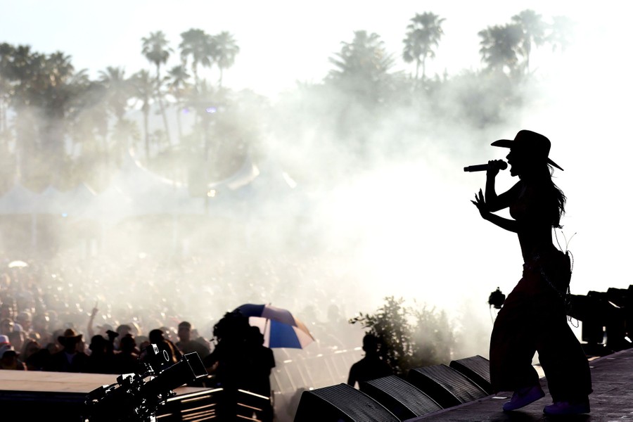 A performer wearing a cowboy hat in silhouette on a stage before a crowd