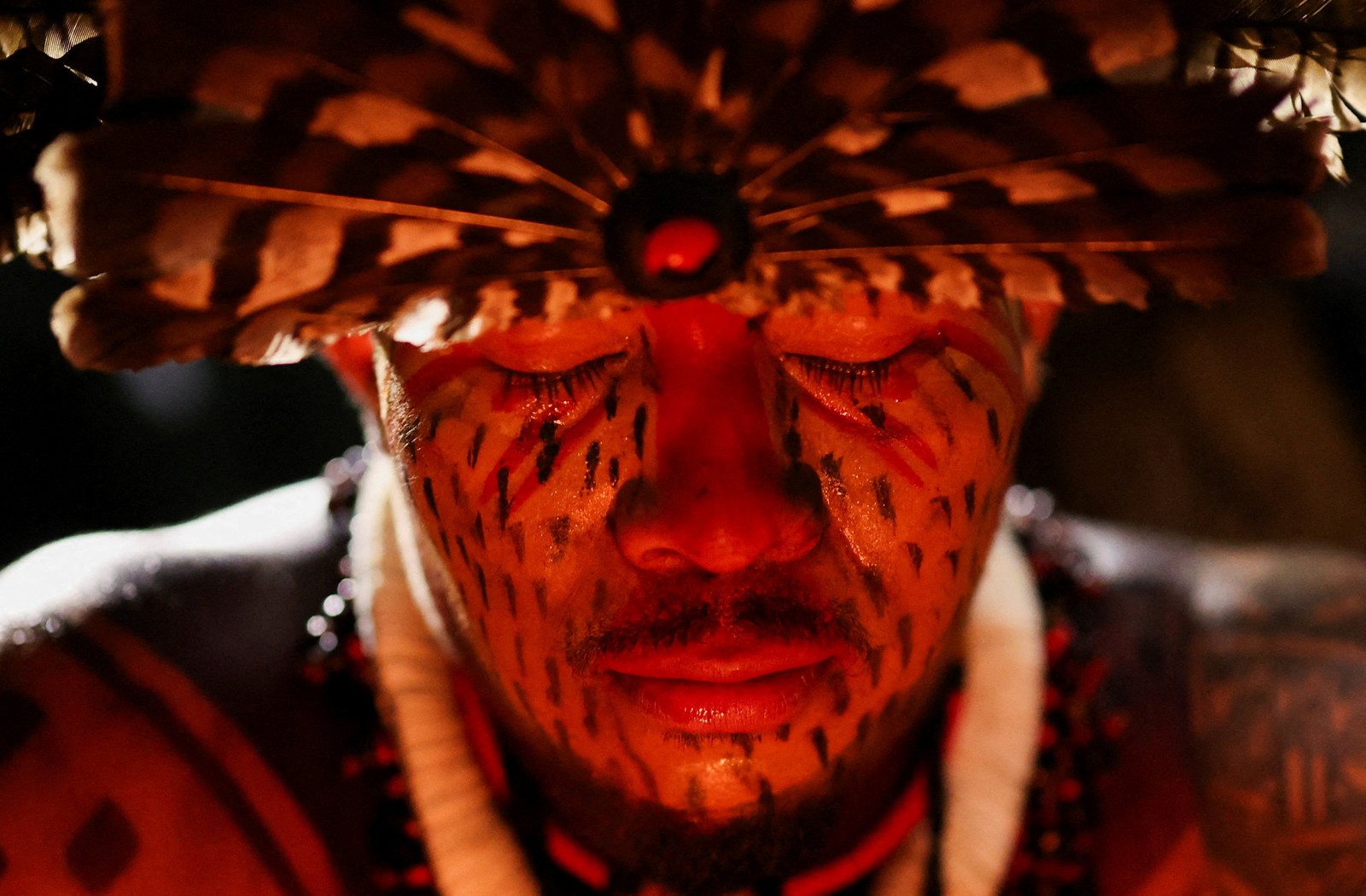 A close view of an Indigenous man wearing a traditional feathered headdress and makeup