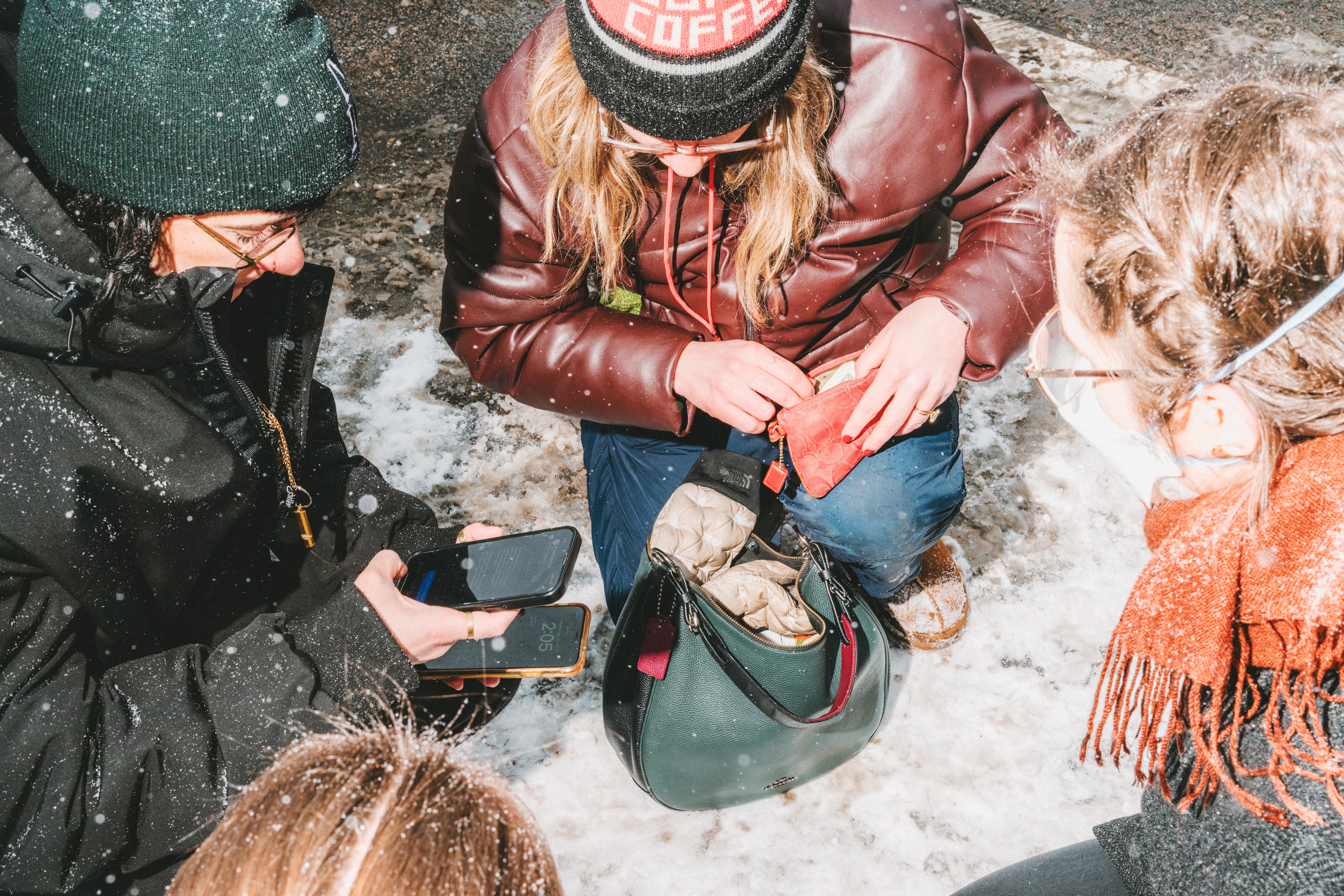 Three women crouch on the ground with their phones during a protest