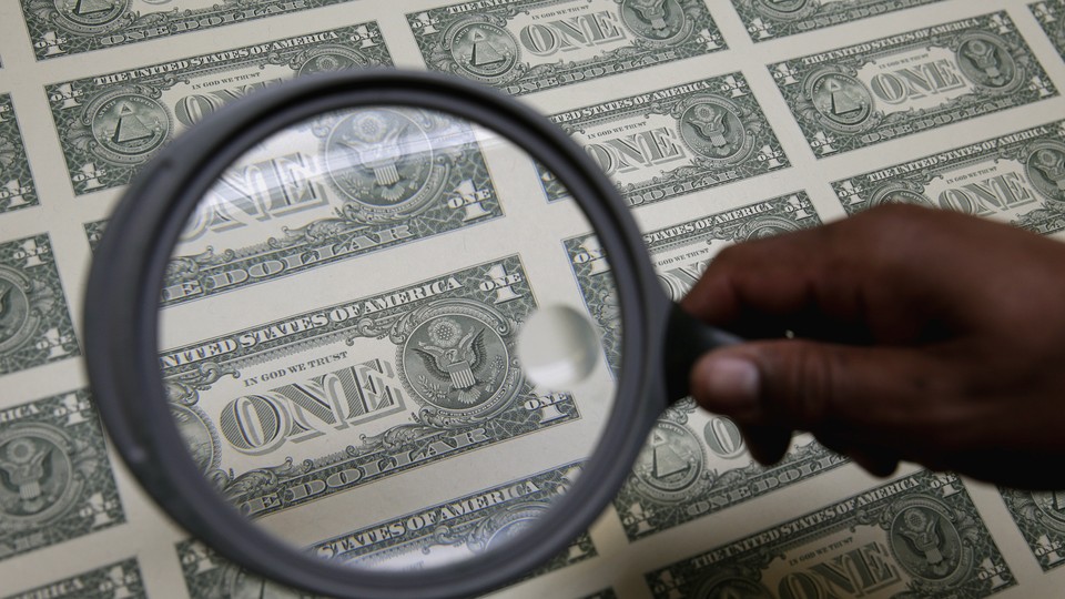 A magnifying glass hovers over a sheet of one-dollar bills.