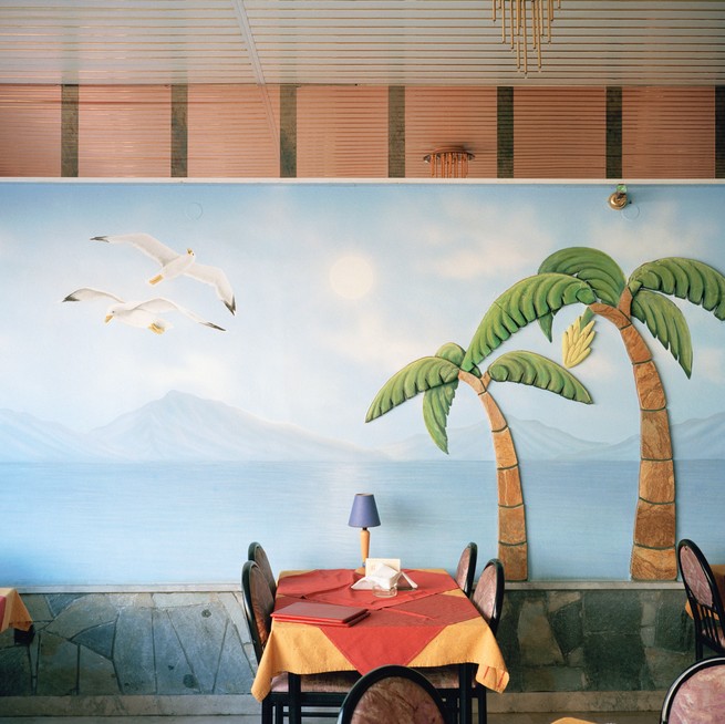 a dining room table in front of a painting of an ocean scene with palm trees and seagulls