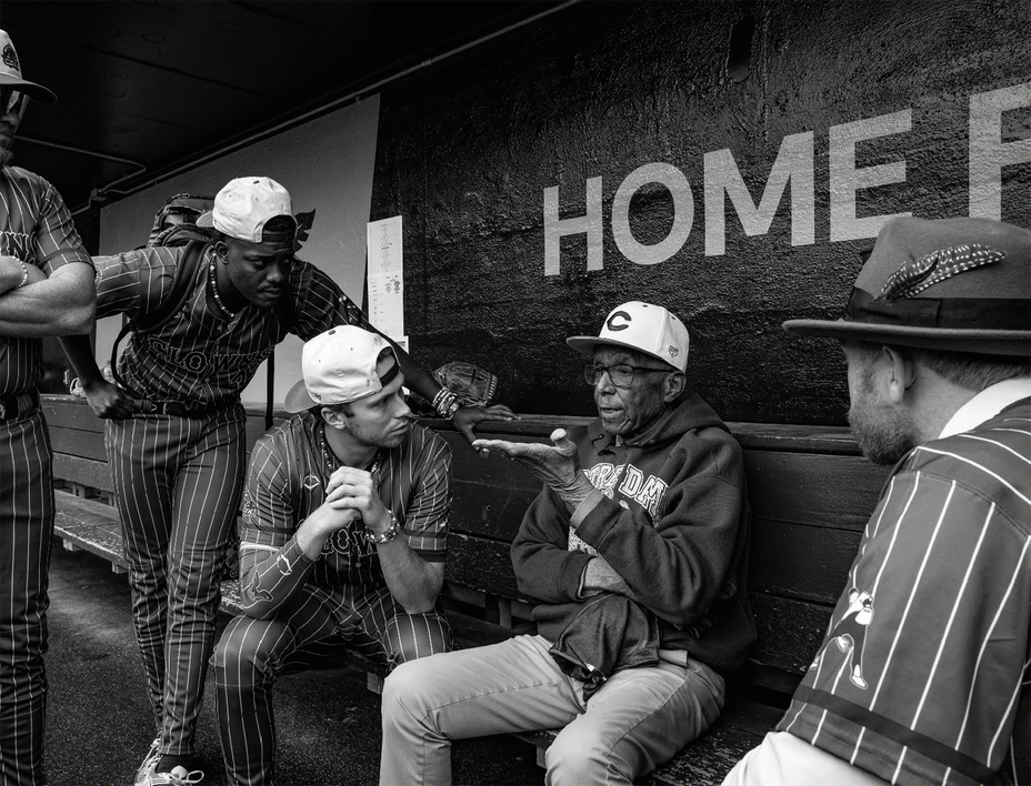 black-and-white photo of older man sitting in dugout surrounded by other players listening to him speak