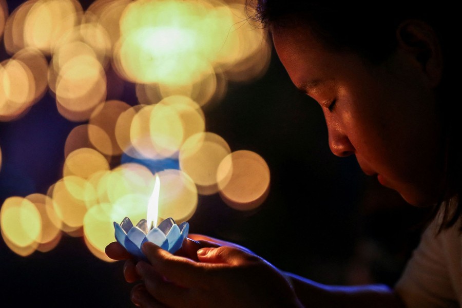 A person holds a small candle in a flower-shaped dish.