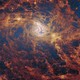 A tight view of the swirling center of a distant spiral galaxy, dominated by billowing yellowish-orange streams of gas and dust