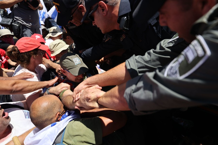 Several security officers lean over, pulling on a protester who is held down by other protesters around him.