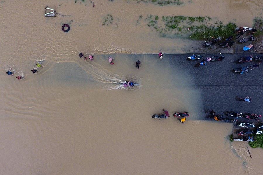 An aerial photo of people walking and riding motorcycles on a flooded road.