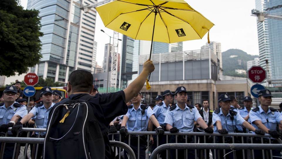 A pro-democracy protester rises a yellow umbrella, the symbol of the Occupy Central movement, in front of a line of police officers.