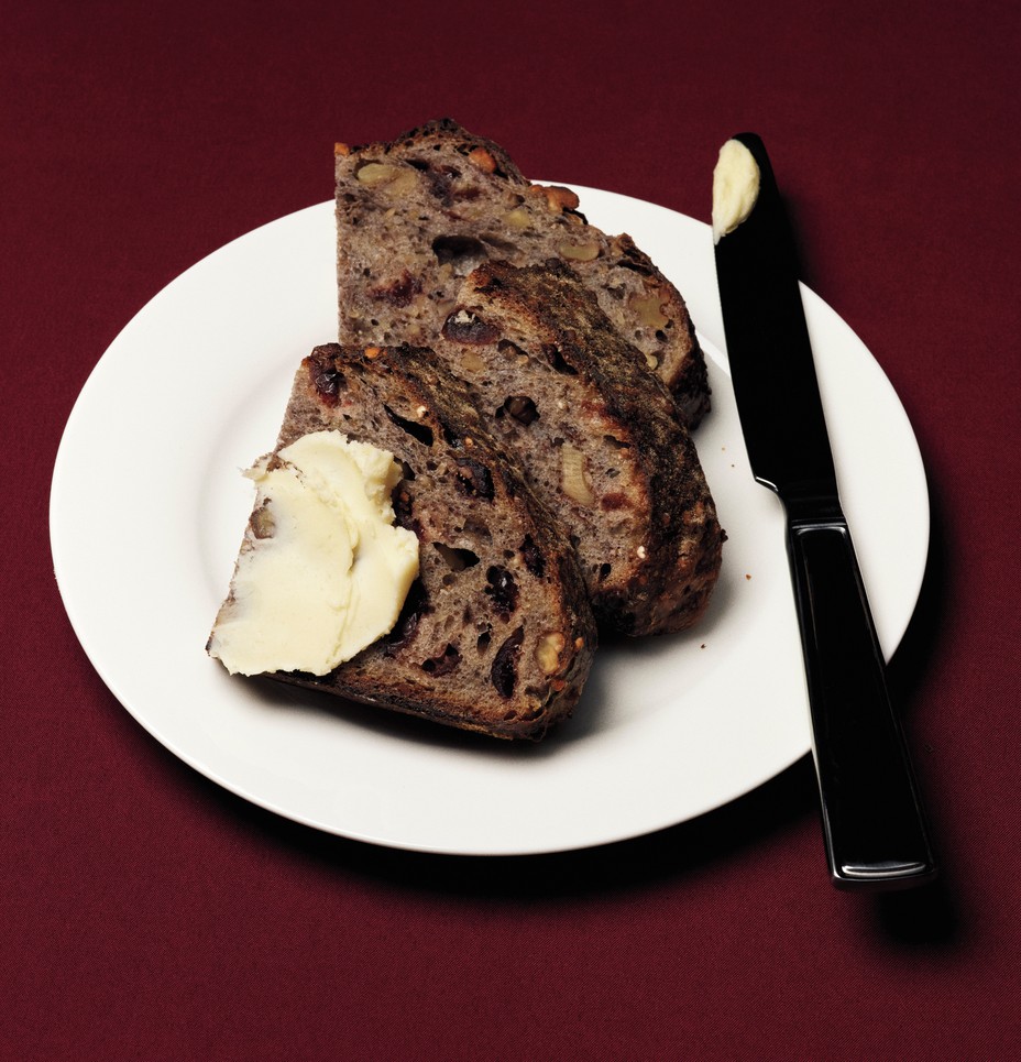 photo of 3 slices of cranberry walnut bread, one slathered with butter, on white plate with burgundy background