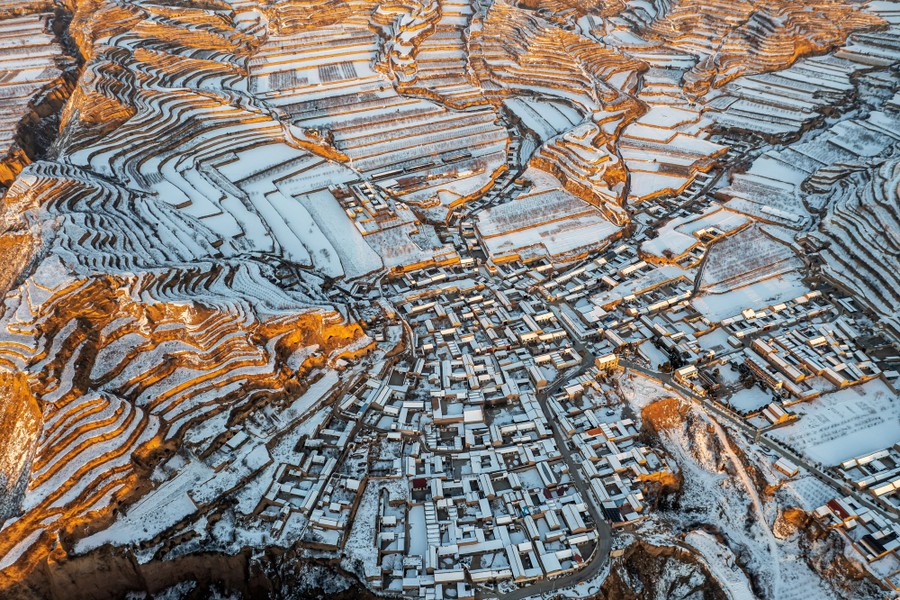 An aerial view of snow-covered terraced fields and buildings