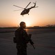 A soldier holding a gun in a helipad at sunset