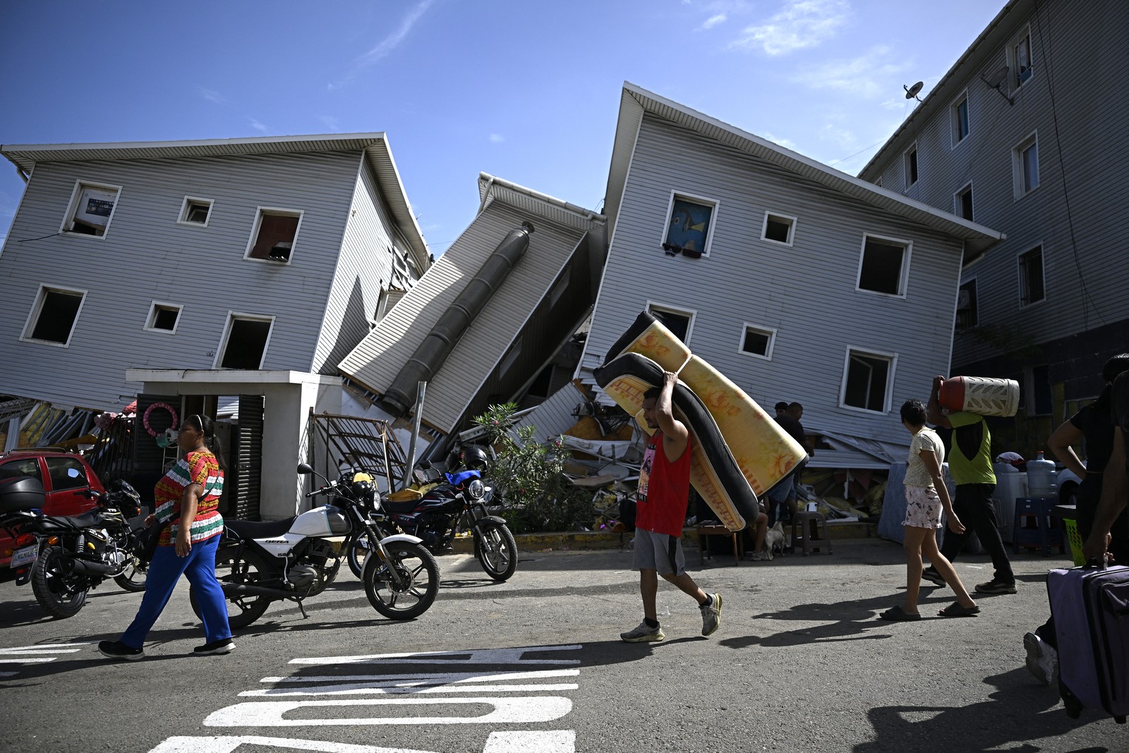 A man carries a mattress past damaged residential buildings following an earthquake.
