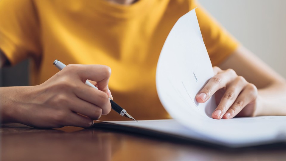 woman in a yellow shirt signing a document with a white pen