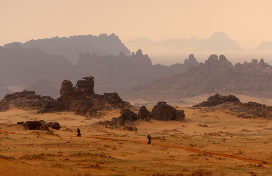 Two motorcycle riders race through a rocky desert landscape.