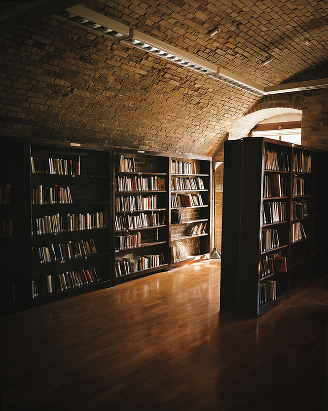 photo of dimly lit room with vaulted stone ceiling and shelves of books, with light coming through a window in background