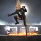 Lady Gaga in midair at her microphone on a stage covered in flames