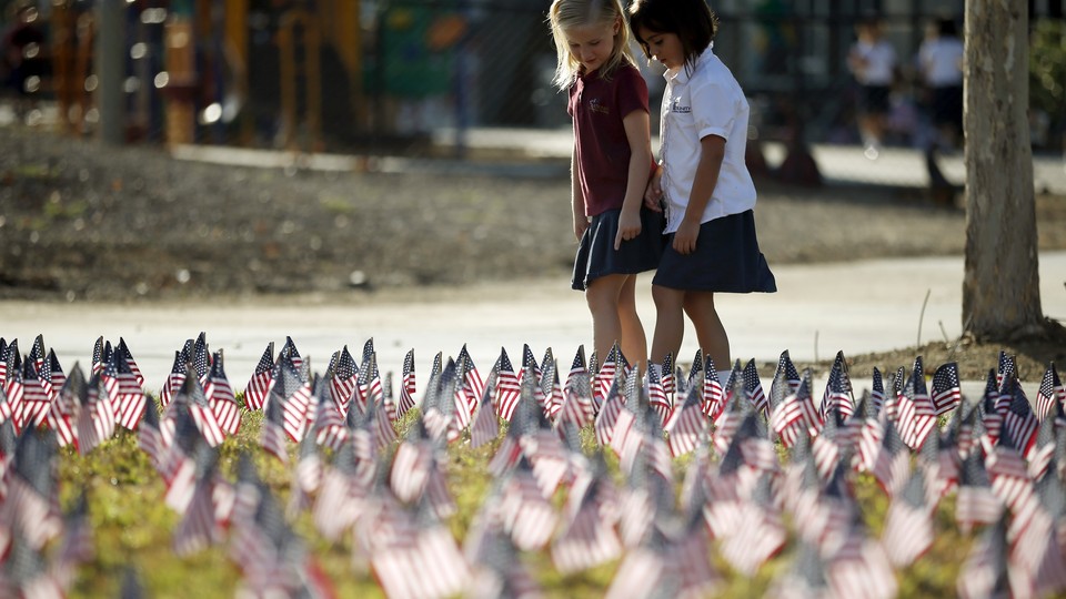 Two girls walk through a field filled with American flags.