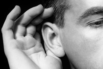 A man cups his hand to his ear