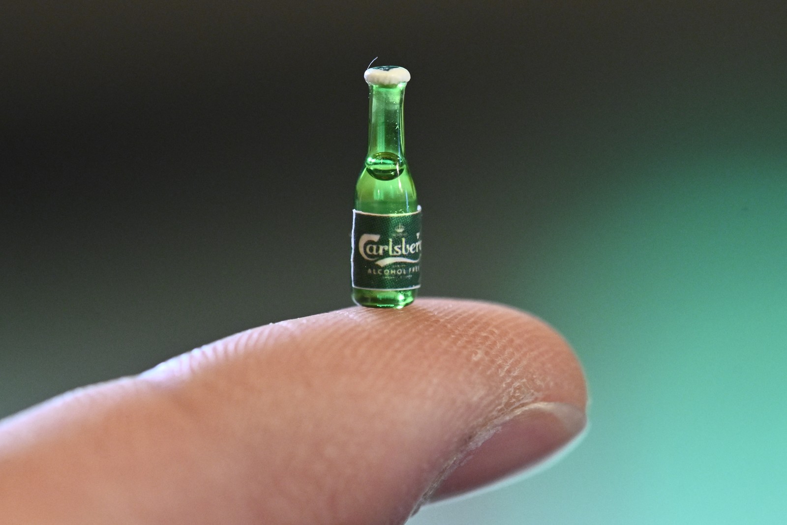 A very tiny bottle of beer, sitting on a fingertip