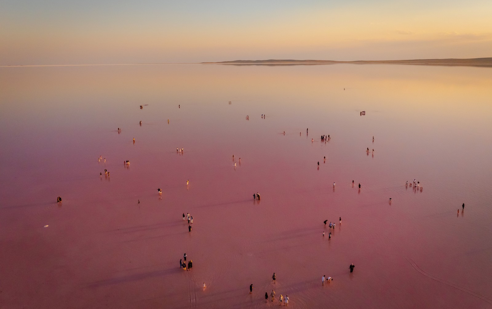 An aerial view of people wading in a shallow and colorful salt lake.