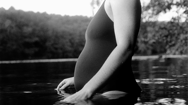 Black-and-white photo of a pregnant person entering a body of water