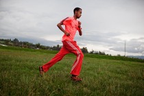 A Black man, dressed in all red workout clothing, running across a grassy field