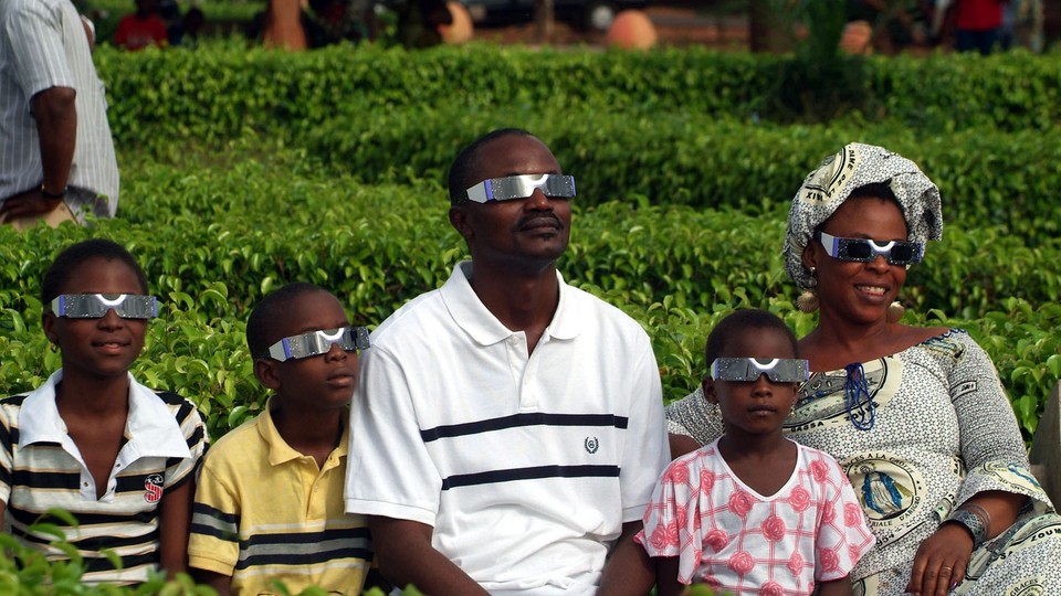 A family looks forward while wearing eclipse glasses.