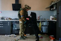 A soldier stands in an abandoned kitchen playing with a dog who is standing on its hind legs in front of him.