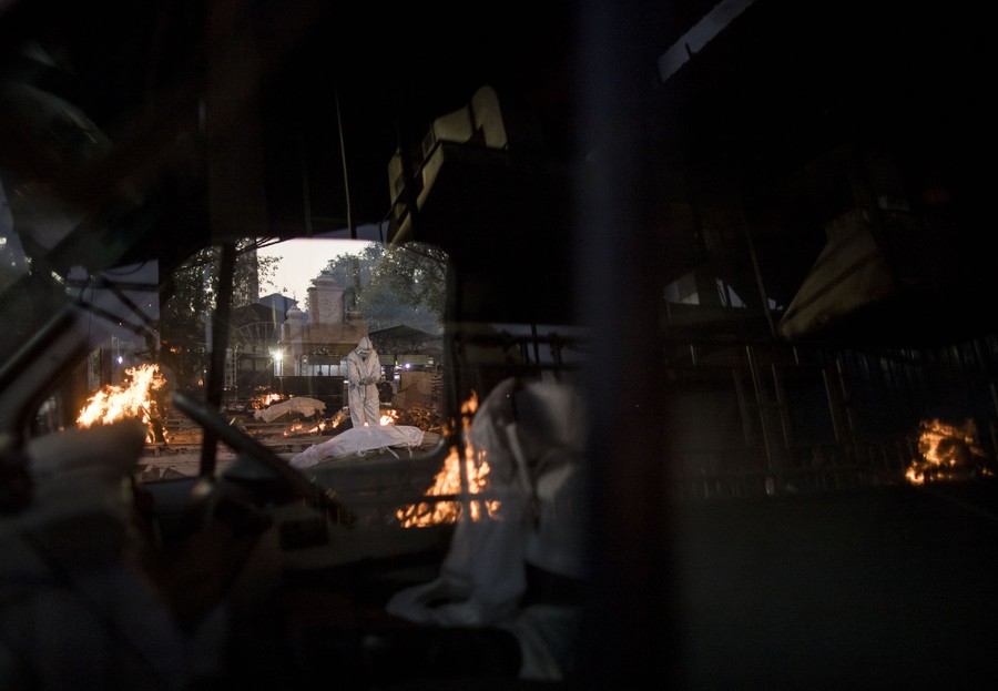 A man performs last rites amid multiple burning pyres in a crematorium.