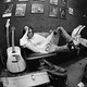 A young Neil Young lying sideways on a couch surrounded by guitars