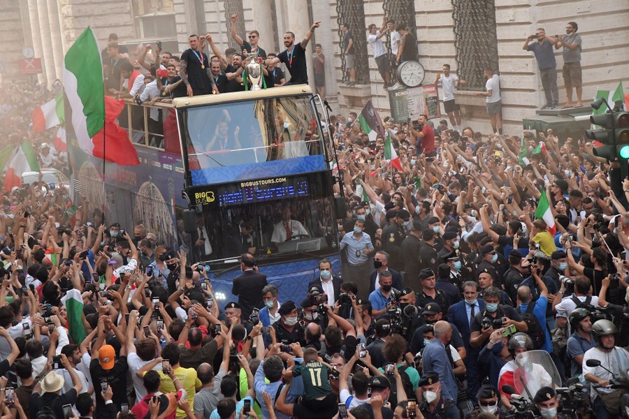 A large crowd of fans surrounds a double-decker bus driving through Rome.