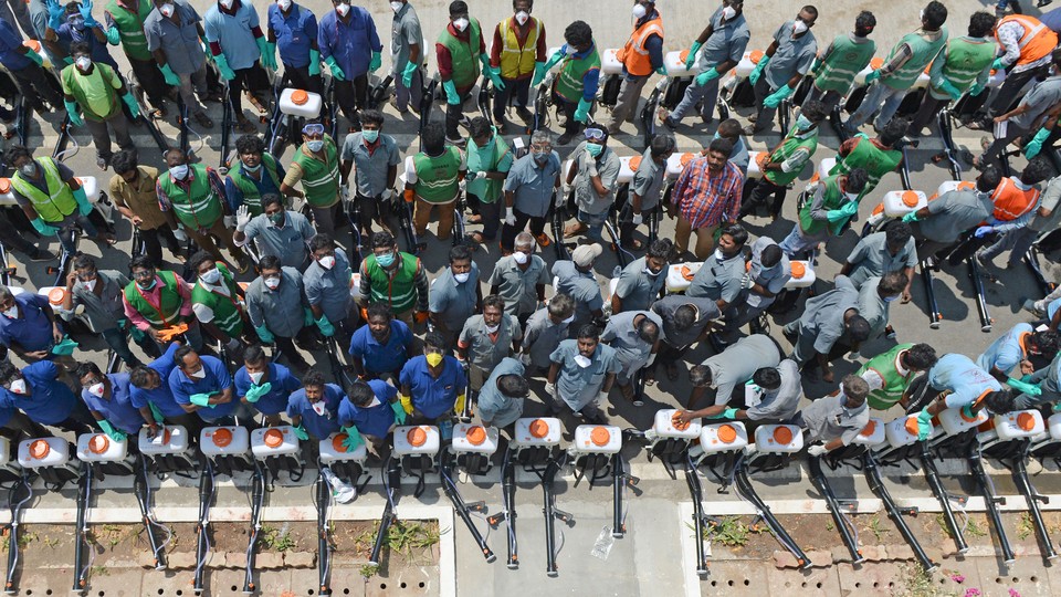 Health workers wearing facemasks amid concerns over the spread of the COVID-19 novel coronavirus, stand as they wait to spray disinfectant at the corporation office in Chennai on March 20, 2020.