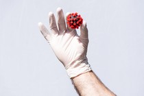 A white gloved hand holds a COVID-19 virus