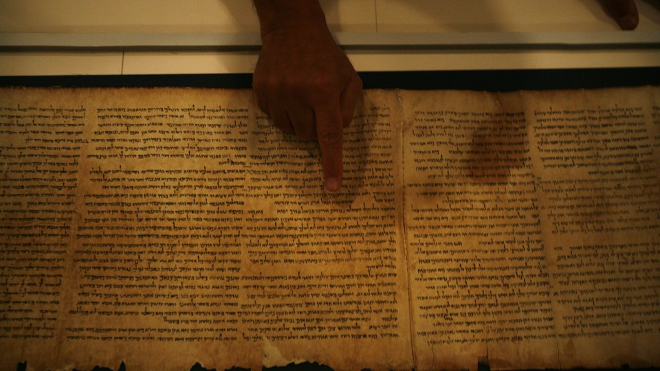 A person points with their index finger at the Isaiah Scroll.