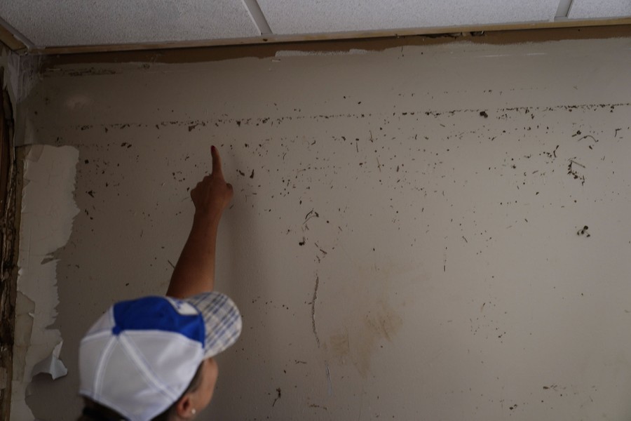 A person points to debris left high on a wall, indicating the height of the previous floodwater.