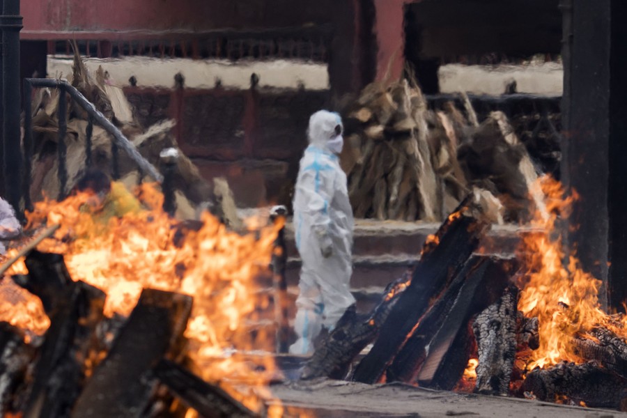 A man wearing protective equipment stands among burning pyres.