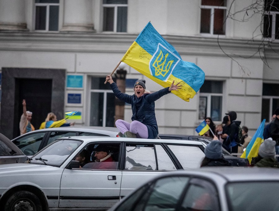 People wave blue-and-yellow flags, celebrating in the street and on a car.