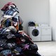 A towering pile of laundry next to a washing machine