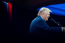 Donald Trump speaking into a microphone, gesturing his right arm forward