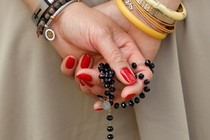 Color photo of a woman holding a rosary with her hands draped behind her back.