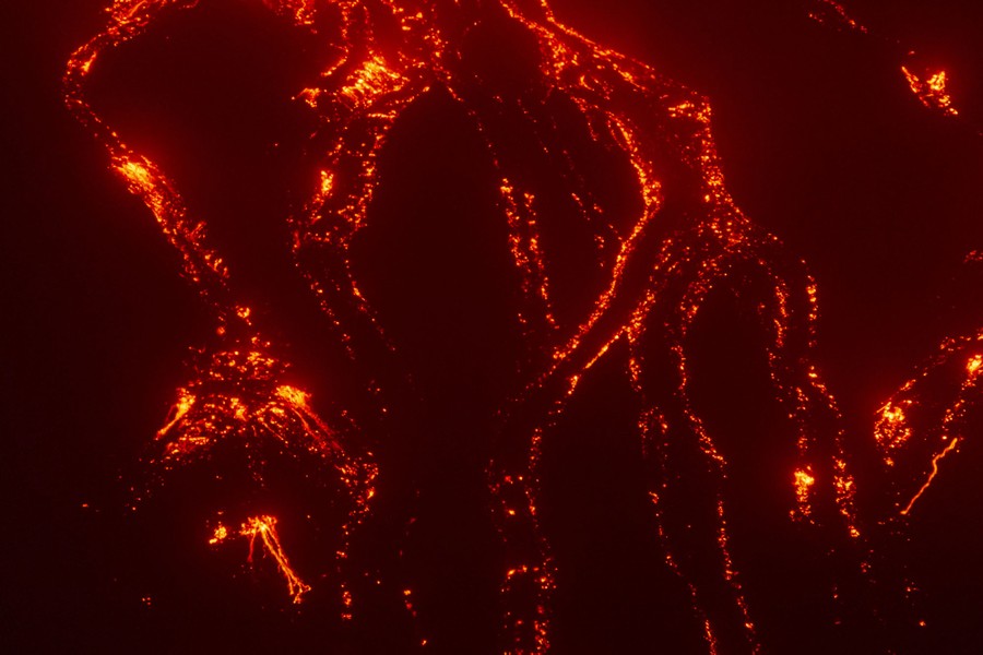 A nighttime view of several branches of flowing lava on a mountainside