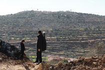 A man stands on a hillside with a young boy, pointing into the distance