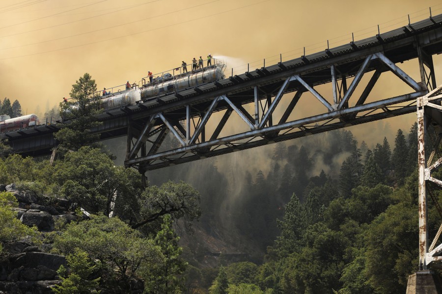 Firefighters spray water from a fire train on a tall bridge.