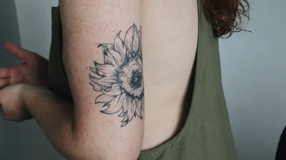 A tattoo of a flower on a young woman's upper arm