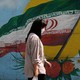 A woman walks in front of a mural of the Iranian flag