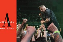 Ken Casey, front man of the Dropkick Murphys holds a microphone up to his mouth while reaching into the crowd at a concert