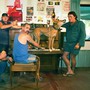 A group of men raise their beers while a dingo stands on a piano and howls.
