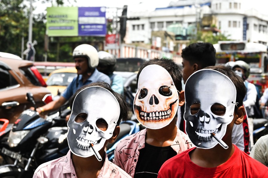 Three young people wearing skeleton masks stand alongside a road.