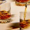 photo of brown liquor being poured over ice into multiple highball glasses